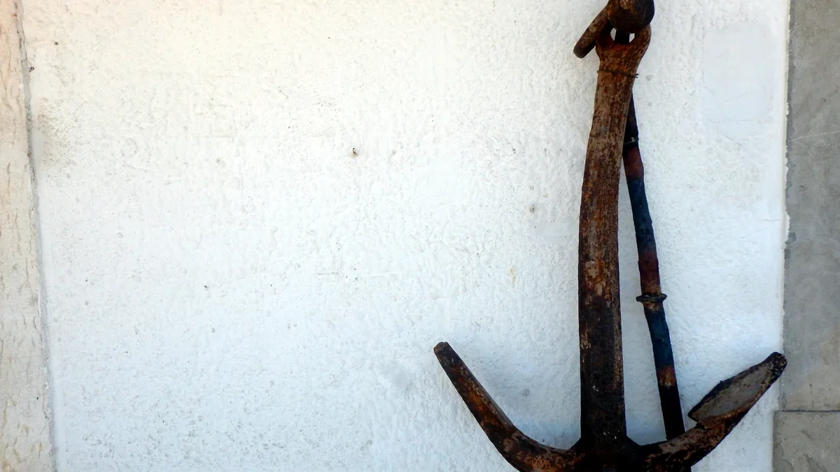 A rusted iron anchor mounted on a wall in a maritime museum hall, lit by soft window light.